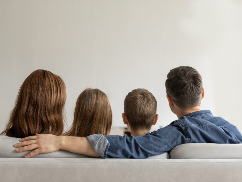 An image capture of a family moment where a family of four are sitting close on a sofa, showing unity and affection