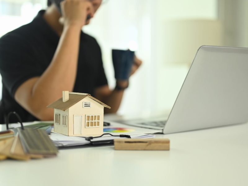 Small house model and color swatches on desk representing architectural design or real estate development.